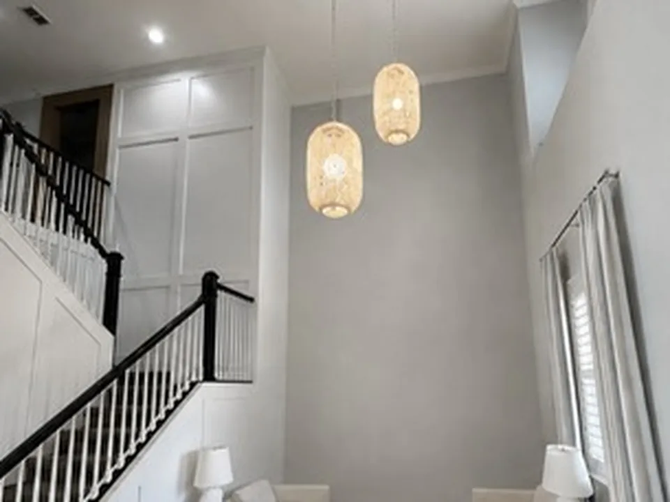Two-story living room with a tall bare grey wall beneath woven pendant lights, beside a white staircase