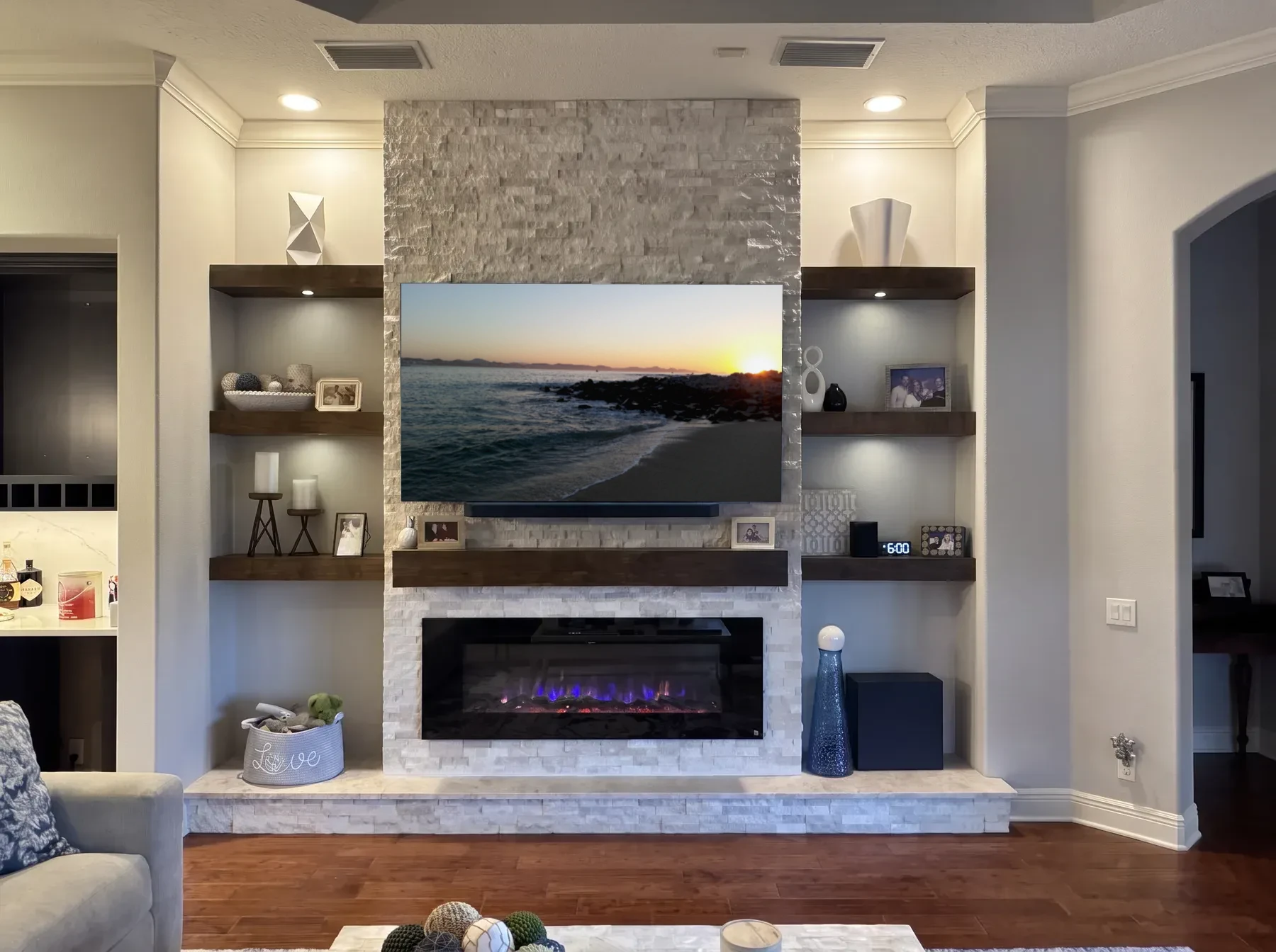 Light stacked stone column with floating walnut shelves, a timber mantel and a linear fireplace above a stone hearth