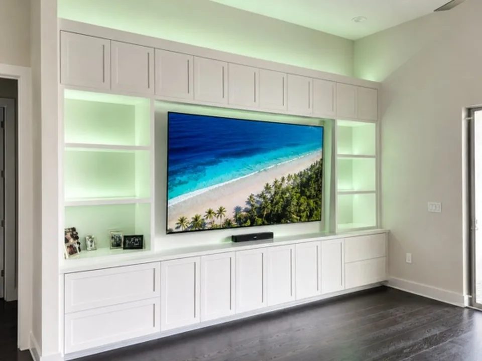 Wall-to-wall white built-in with upper cabinets, green LED-lit open shelving around a recessed television and a long run of base cabinets