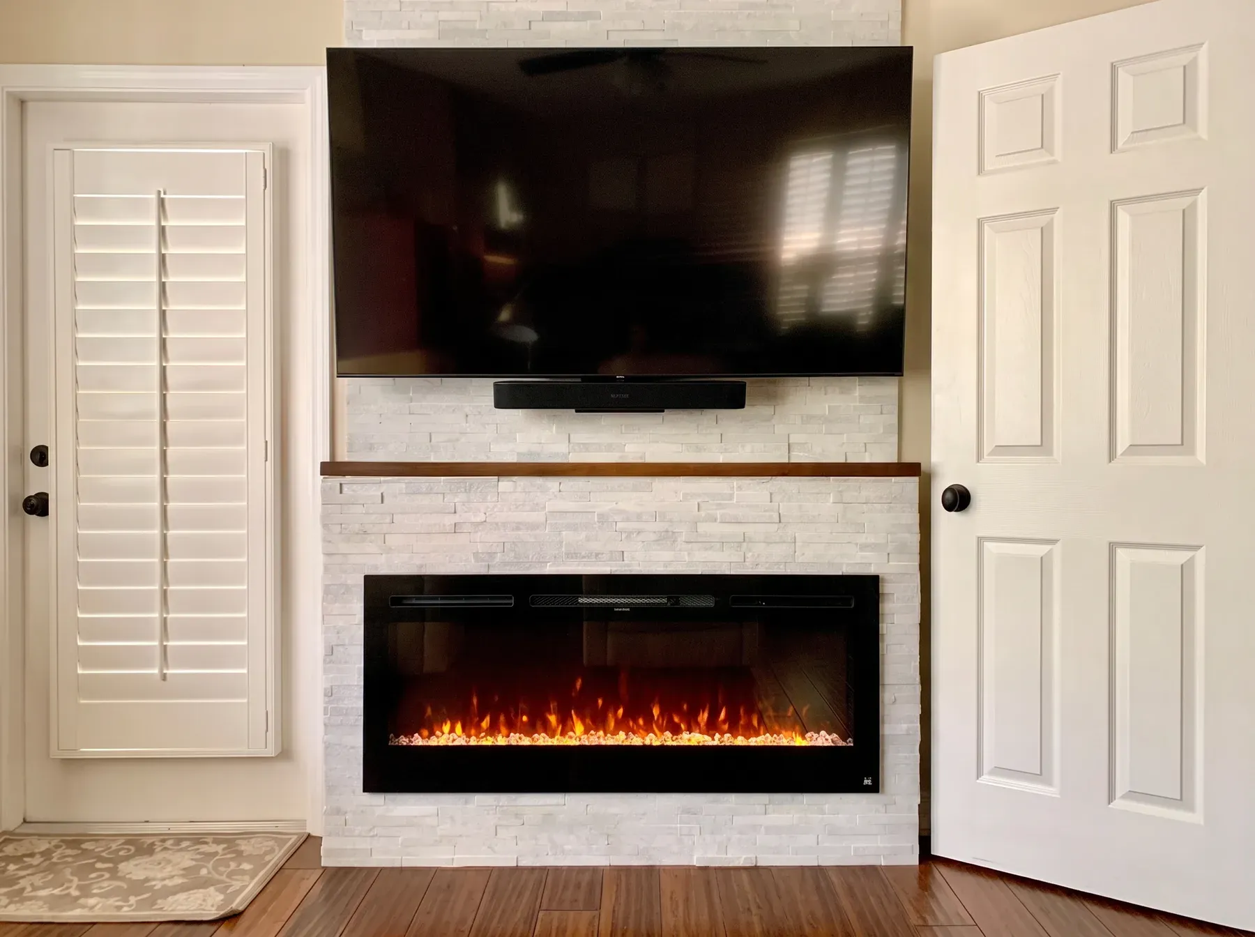 White stacked stone wall with a walnut mantel shelf, linear fireplace and wall-mounted television